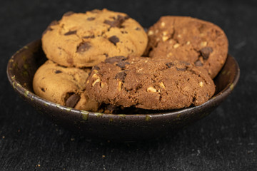 Group of four whole sweet brown cookie in glazed bowl flatlay on grey stone
