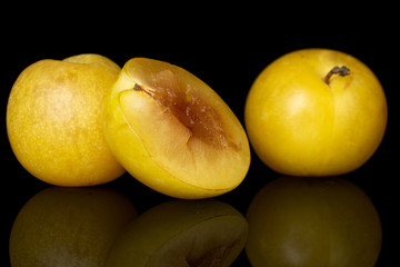 Group of two whole one half of fresh yellow plum isolated on black glass