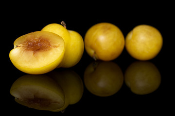 Group of three whole one half of fresh yellow plum isolated on black glass