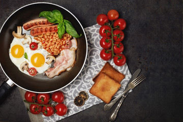 English breakfast. Fried eggs, sausages, bacon, beans, toasts, tomatoes on stone table. Top view with copy space