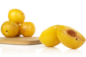 Group of four whole two halves of fresh yellow plum on bamboo cutting board isolated on white background