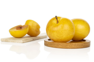 Group of two whole two halves of fresh yellow plum on round bamboo coaster on wooden cutting board isolated on white background