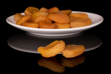 Lot of whole dried orange apricot front focus on white ceramic plate isolated on black glass