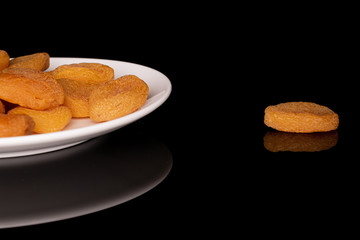 Lot of whole dried orange apricot one in focus on white ceramic plate isolated on black glass