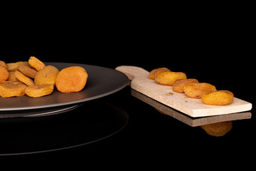 Lot of whole dried orange apricot on gray ceramic plate on wooden cutting board isolated on black glass
