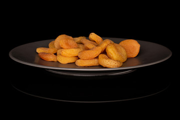 Lot of whole dried orange apricot on gray ceramic plate isolated on black glass