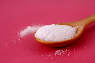 Salt on a wooden spoon on a pink background.