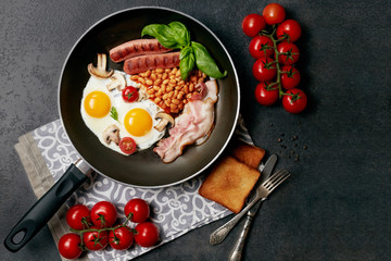English breakfast. Fried eggs, sausages, bacon, beans, toasts, tomatoes on stone table. Top view with copy space