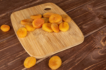 Lot of whole dried orange apricot on bamboo cutting board on brown wood