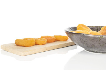 Lot of whole dried orange apricot on wooden cutting board in glazed bowl isolated on white background