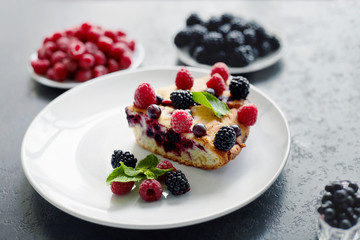 Piece of pie with blueberries, raspberry and mint for dessert on a white plate. Pieces of delicious homemade cake on a background