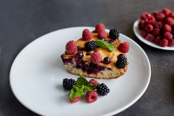Piece of pie with blueberries, raspberry and mint for dessert on a white plate. Pieces of delicious homemade cake on a background
