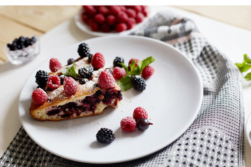 Piece of pie with blueberries, raspberry and mint for dessert on a white plate. Pieces of delicious homemade cake on a background