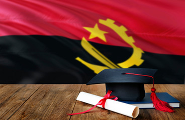Angola education concept. Graduation cap and diploma on wooden table, national flag background. Succesful student.
