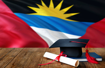 Antigua and Barbuda education concept. Graduation cap and diploma on wooden table, national flag background. Succesful student.