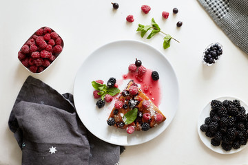 Piece of pie with blueberries, raspberry and mint for dessert on a white plate. Pieces of delicious homemade cake on a background