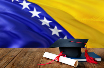 Bosnia Herzegovina education concept. Graduation cap and diploma on wooden table, national flag...