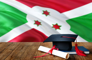Burundi education concept. Graduation cap and diploma on wooden table, national flag background. Succesful student.