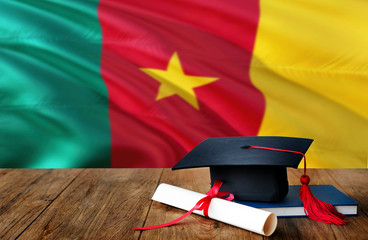 Cameroon education concept. Graduation cap and diploma on wooden table, national flag background. Succesful student.