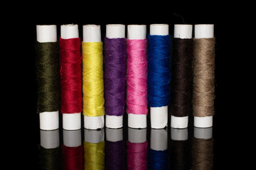 Group of eight whole upright sewing thread spool isolated on black glass