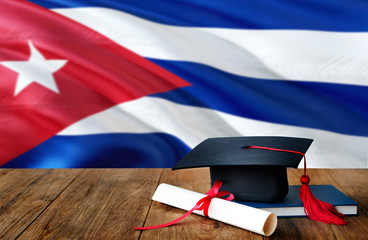 Cuba education concept. Graduation cap and diploma on wooden table, national flag background. Succesful student.