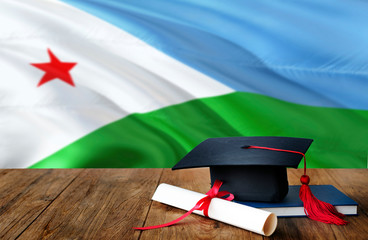 Djibouti education concept. Graduation cap and diploma on wooden table, national flag background. Succesful student.