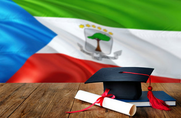 Equatorial Guinea education concept. Graduation cap and diploma on wooden table, national flag background. Succesful student.