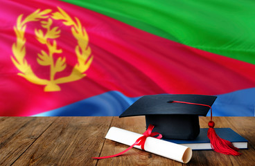 Eritrea education concept. Graduation cap and diploma on wooden table, national flag background. Succesful student.