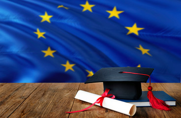 European Union education concept. Graduation cap and diploma on wooden table, national flag...