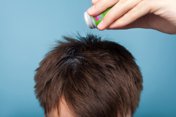 Fototapeta premium Closeup of male hand applying medications on brunette male hair, treating premature hair loss or dandruff, lice problem, healthcare and treatment. indoor studio shot isolated on blue background