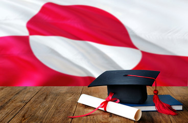 Greenland education concept. Graduation cap and diploma on wooden table, national flag background. Succesful student.