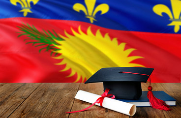 Guadeloupe education concept. Graduation cap and diploma on wooden table, national flag background. Succesful student.