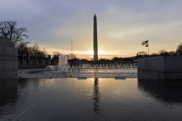 Obraz premium Beautiful sunrise behind America's national monument, the Washington Monument with National WWII Memorial & Rainbow Pool in the foreground