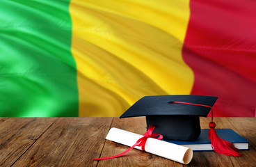 Mali education concept. Graduation cap and diploma on wooden table, national flag background....