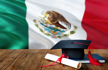 Mexico education concept. Graduation cap and diploma on wooden table, national flag background....
