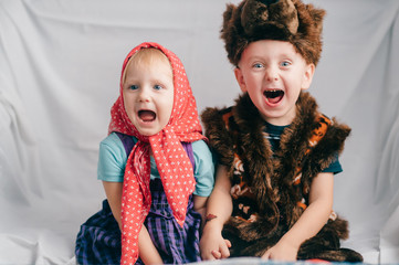 Beautiful couple of lovely children in bear costume and russian cartoon clothes sitting on bed with funny faces. Soft focus portrait of little children in costumes