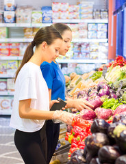 Teen girls shopping in supermarket reading product information. Choosing daily product.Concept of healthy food, bio, vegetarian, diet.