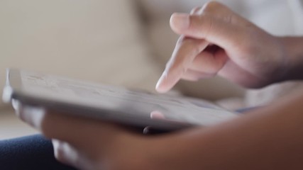 Hand of little girl using digital tablet to learn while sitting on the sofa in the living room at home - Powered by Adobe