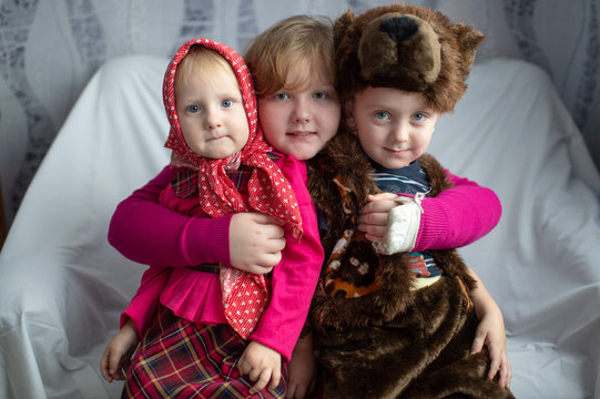 Portrait of beautiful girl hugs her little brother in bear costume and funny young sister in russian style festive dress.  Happy childhood.