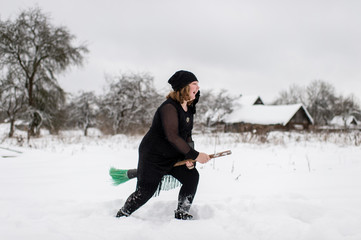 Excited girl dressed in with costume starting to gly on her broomstick to coven in snowy winter day...
