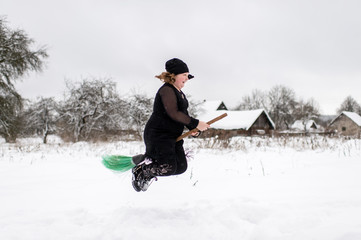 Excited girl dressed in with costume starting to gly on her broomstick to coven in snowy winter day...