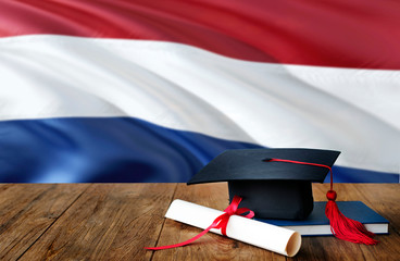 Netherlands education concept. Graduation cap and diploma on wooden table, national flag...