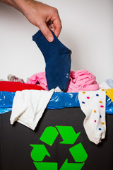 Hand putting used sock in bin with recycling sign. Person in the house separating waste. Heap of...