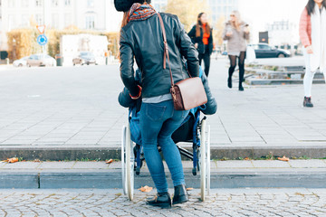 rear view of a woman helping a disabled person to go down the steps with the wheelchair - architectural boundaries in the cities concept
