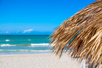 Fototapeta na wymiar Straw umbrella on a beach. Vacation background. Idyllic beach landscape.
