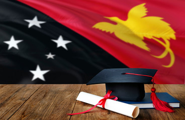 Papua New Guinea education concept. Graduation cap and diploma on wooden table, national flag background. Succesful student.