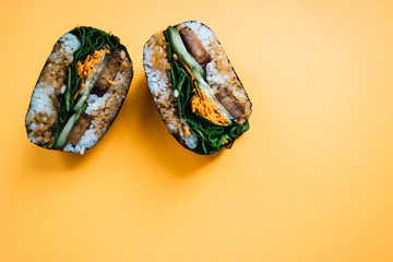 Onigirazu with tempeh, spinach, carrot, cucumber and sesame sauce  on orange background. Japanese food. Top view.