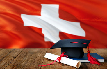 Switzerland education concept. Graduation cap and diploma on wooden table, national flag...