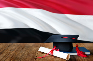 Yemen education concept. Graduation cap and diploma on wooden table, national flag background. Succesful student.