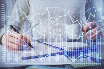 Forex chart hologram on hand taking notes background. Concept of analysis. Double exposure